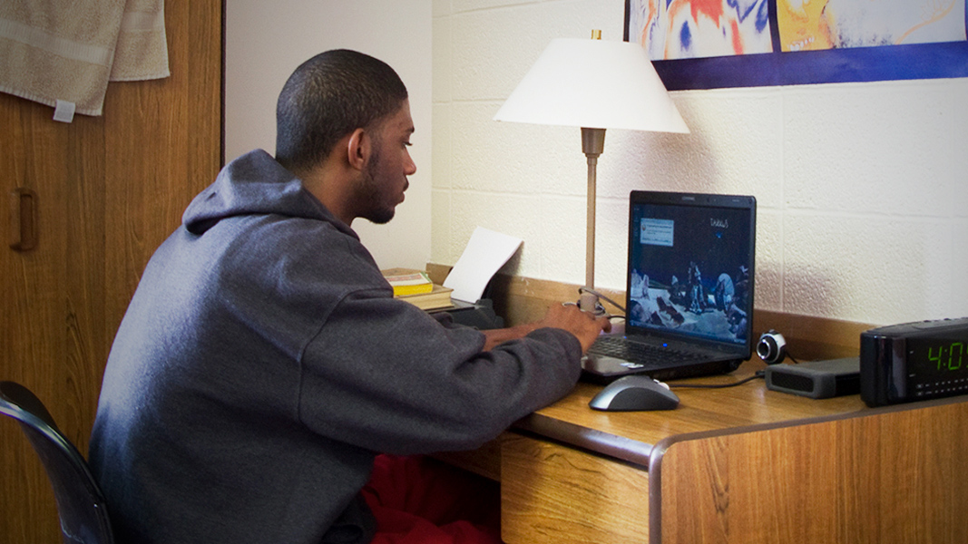 Student doing course work on their laptop in a dorm room