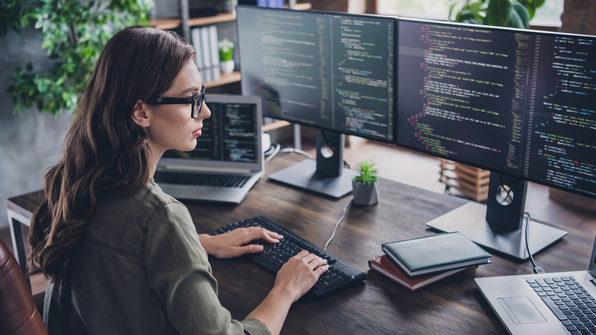 Woman typing html code with several monitors on a desk