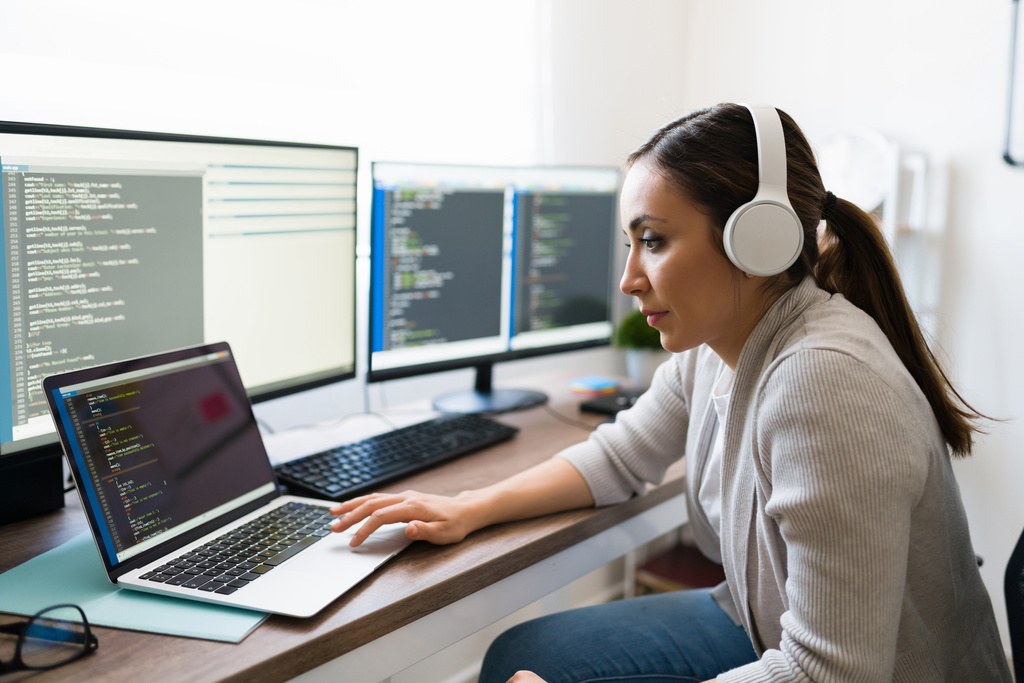 Woman wearing headphones writing code in front of several monitors