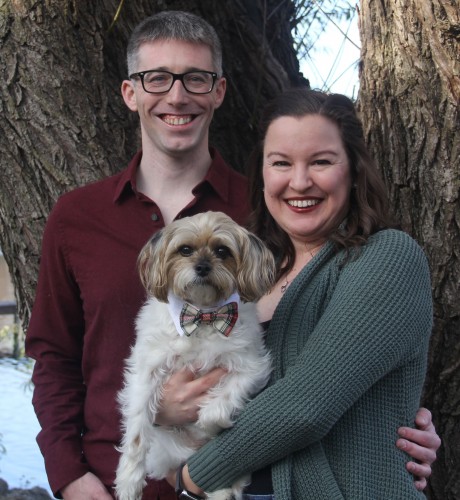 Randi holds her dog, Rax, and stands in front of a tree with her partner, Wally.