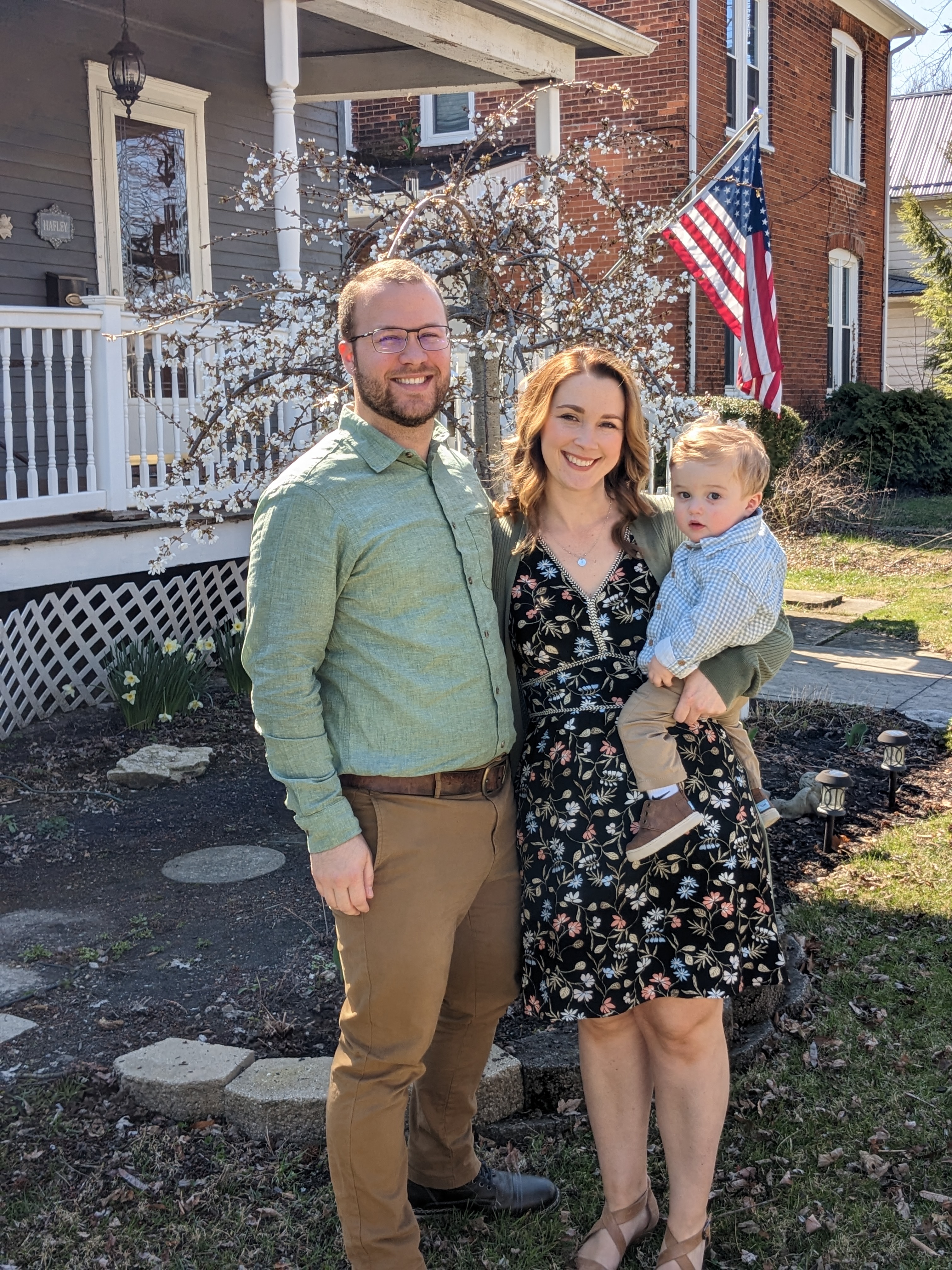 Ben poses with his wife and child in front of their house