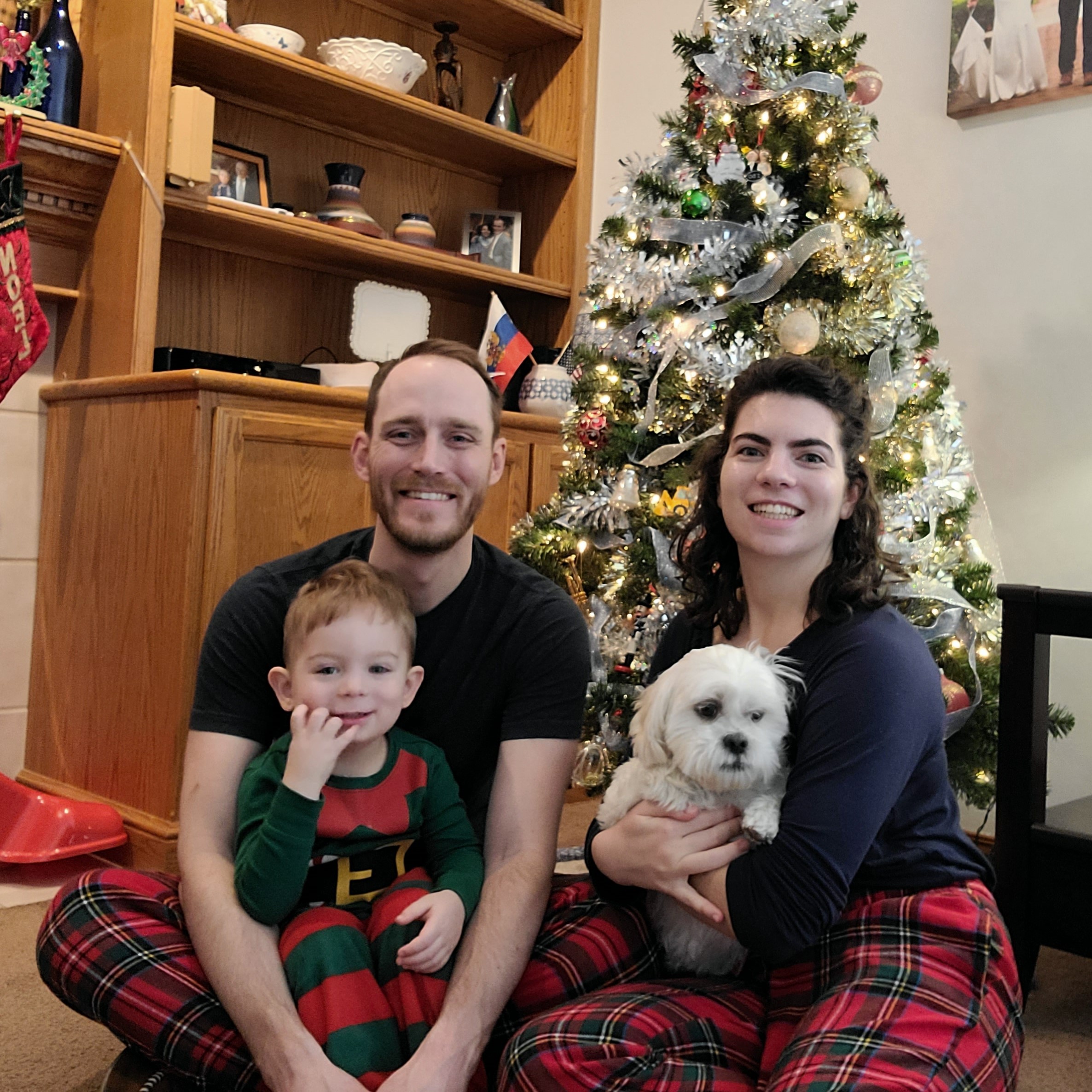 Irina and her husband with their son and dog sitting in front of a Christmas tree.