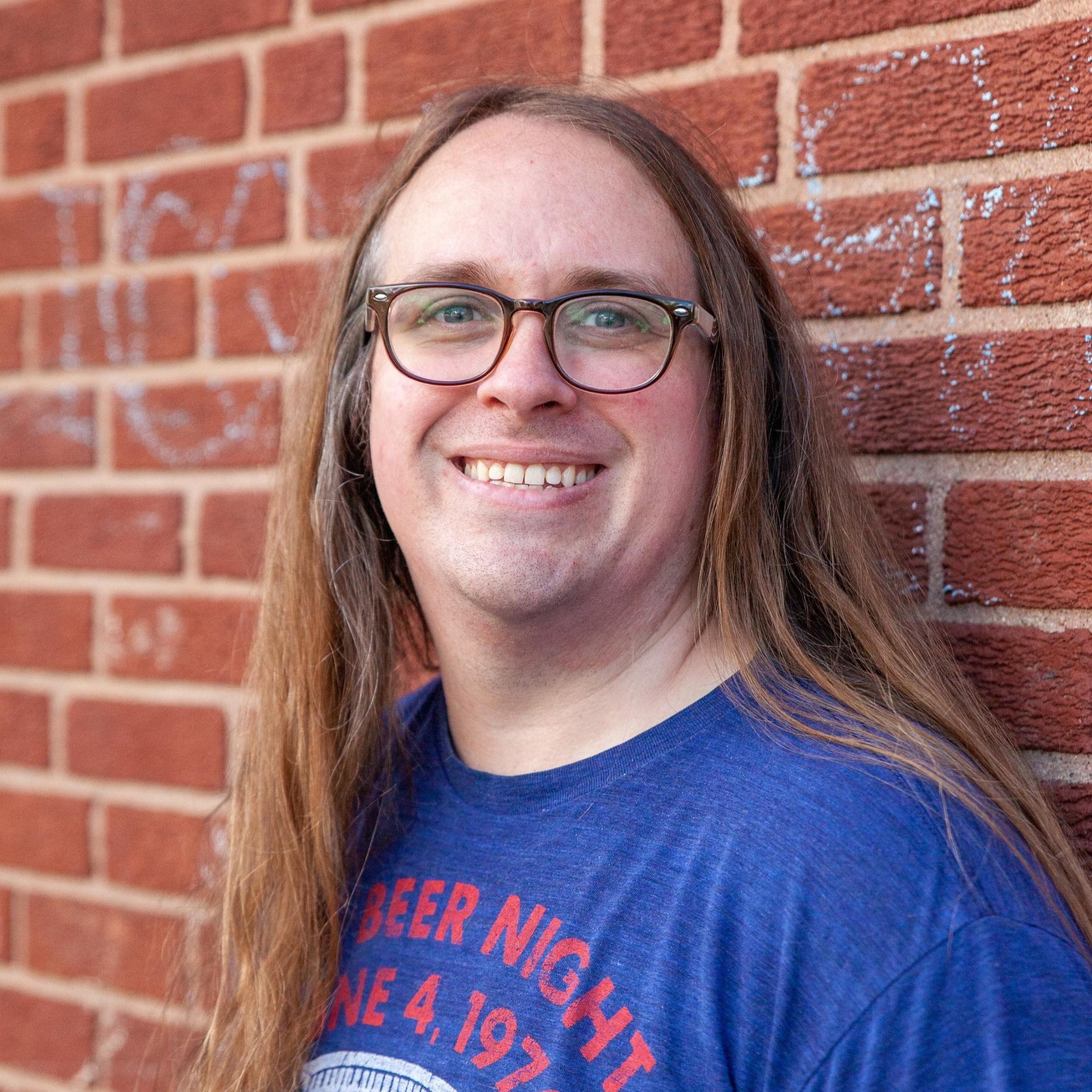 Jimmy smiles in a professional headshot taken against a red brick backdrop.
