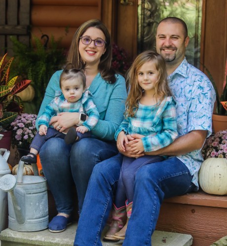 Ashley poses with her husband and two daughters amidst a fun, fall scene