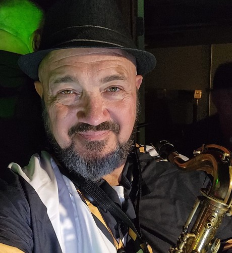 Aaron smiles at the camera while he holds a saxophone.