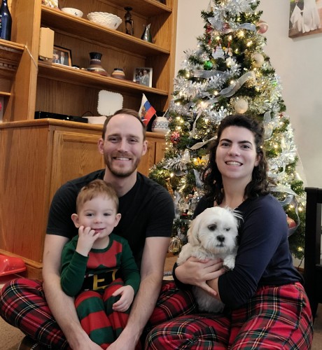 Irina and her husband with their son and dog sitting in front of a Christmas tree.