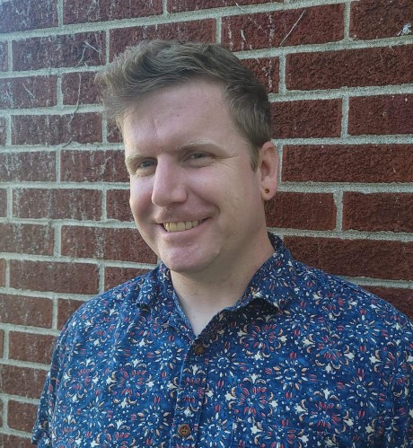 Pat poses for a headshot with a brick wall background