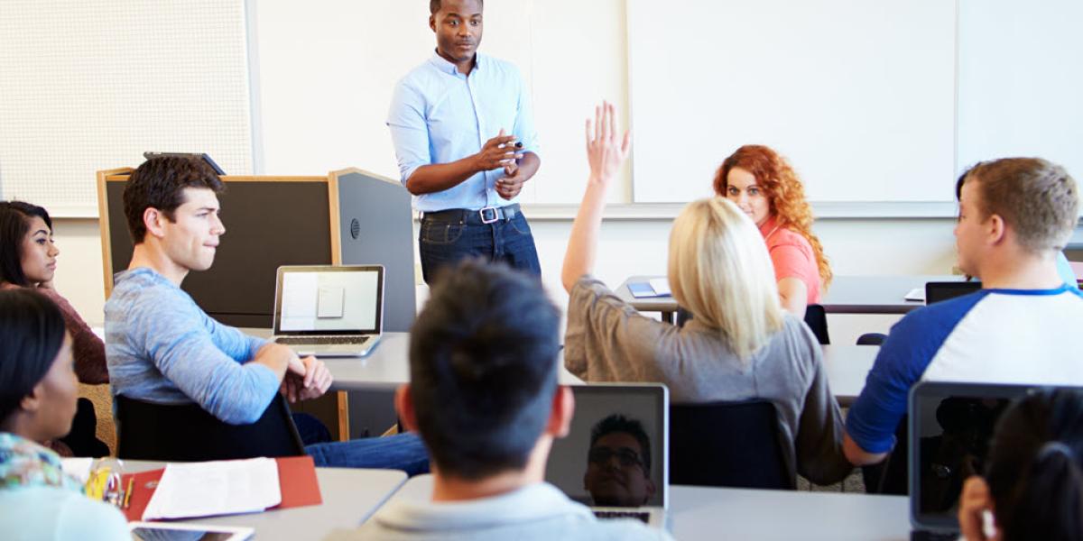 A student raises her hand in the classroom and her instructor points to acknowledge her