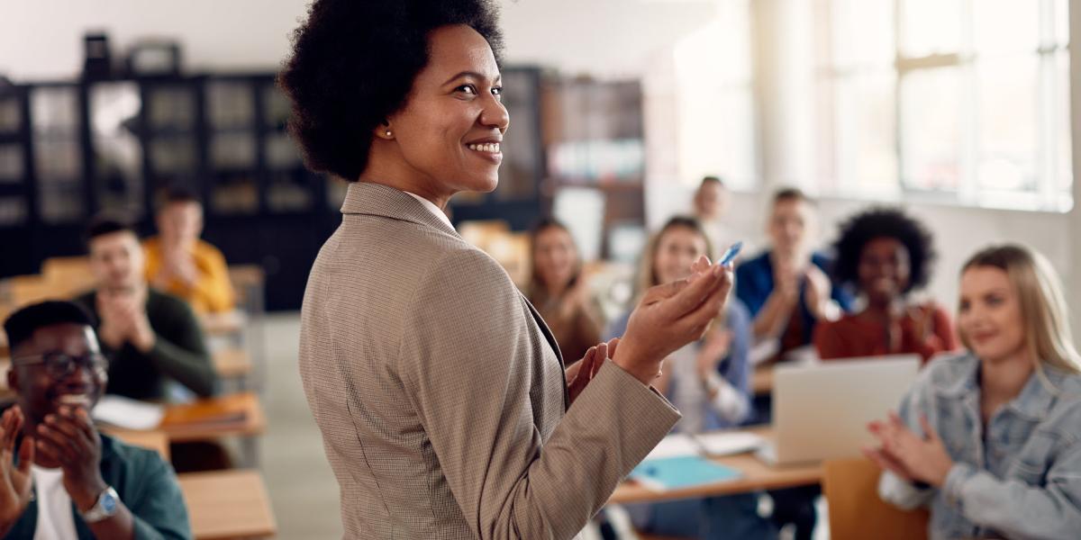 Smiling instructor standing in front of a classroom of students who are clapping