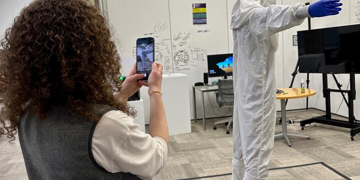 Person using a mobile device to record another person wearing a hazmat suite