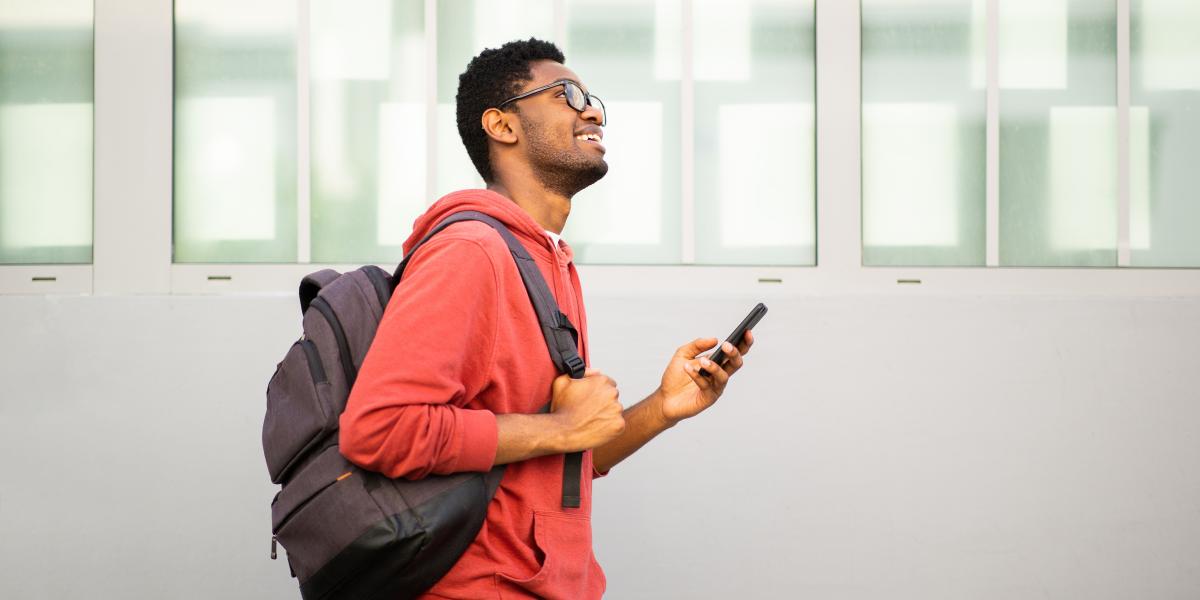 A student wearing a backpack looking at a smartphone while walking.