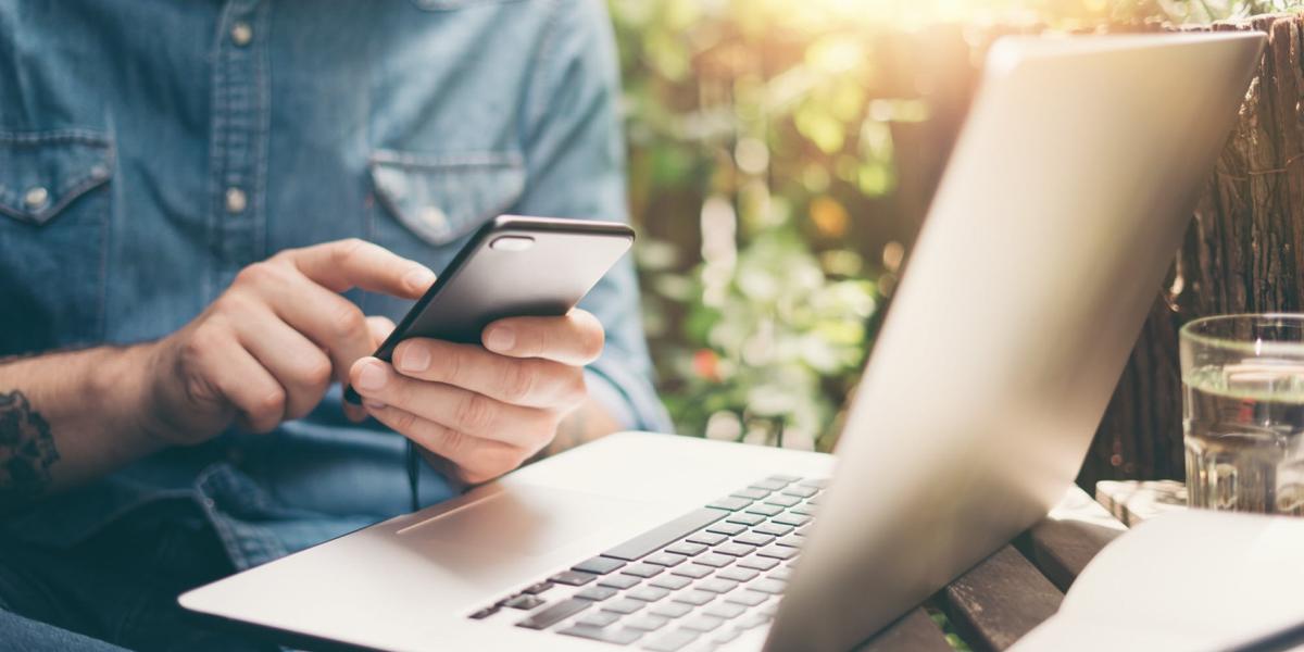 man using a phone in front of an open laptop