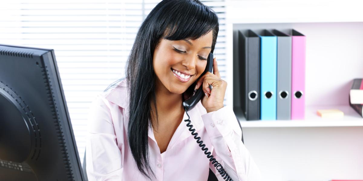 Decorative image of a woman using a corded phone while at a desk in an office