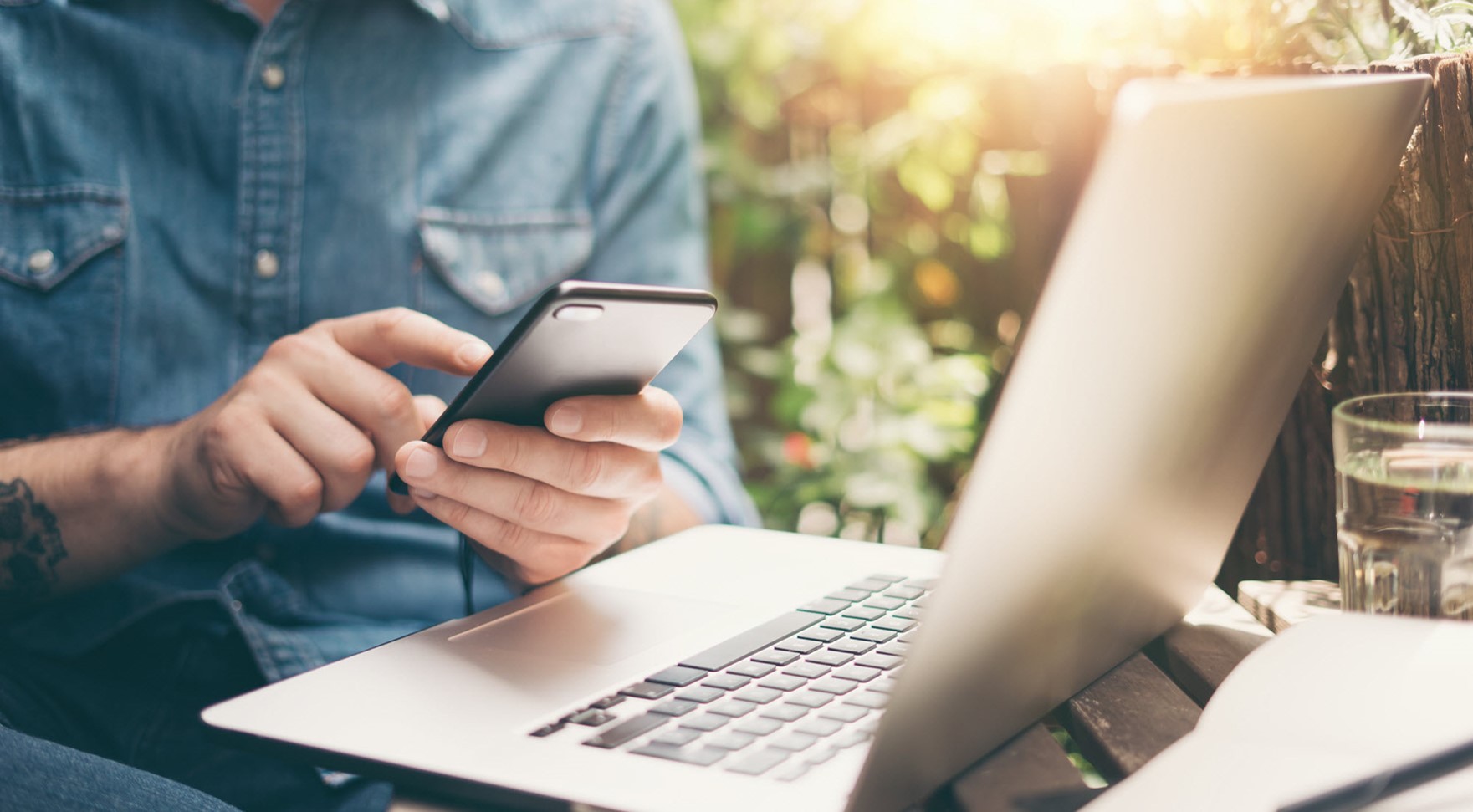 man using a phone in front of an open laptop