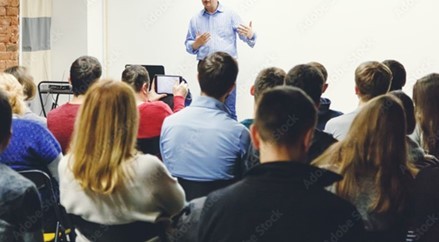 Decorative image of an instructor teaching in an auditorium-style classroom