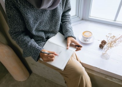 Person writing on a notebook by the windowsill