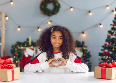 little girl making heart shape with her hands in front of a festive holiday backdrop