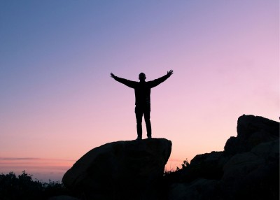 Outline of a person standing on a rock with arms outstretched.