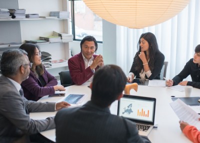 Diverse group of coworkers sitting around a table for an in-person meeting.