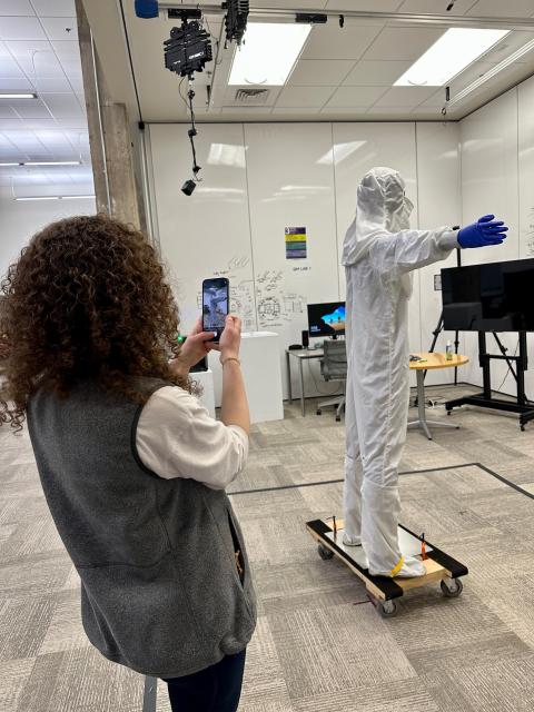 Person using a mobile device to record another person wearing a hazmat suite