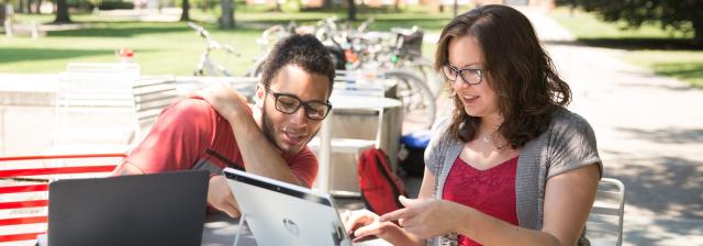 Two people sitting at a table outside looking at a tablet together