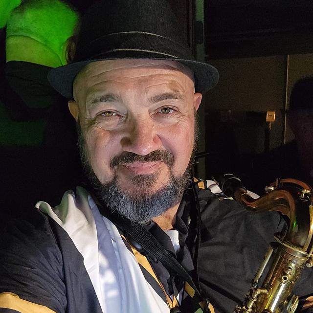 Aaron wearing a hat and holding a saxophone.