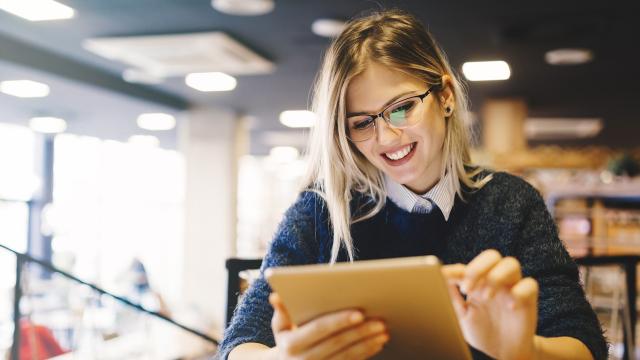 Student smiling while using a tablet in a library