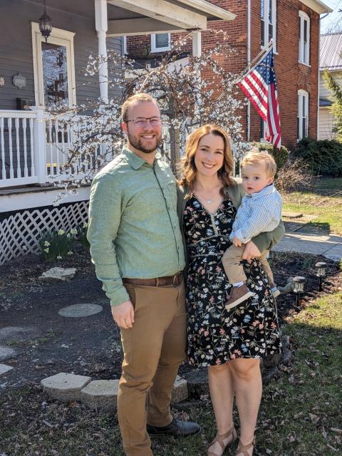 Ben poses with his wife and child in front of their house
