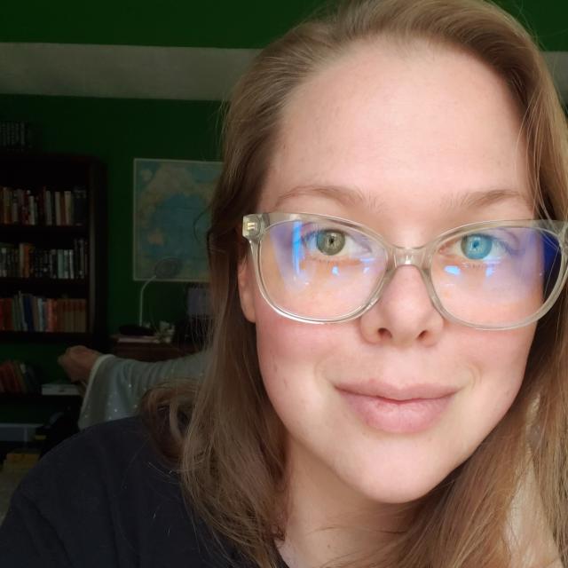A selfie of a young woman, Kaylee, who smirks at the camera and wears clear frame glasses.