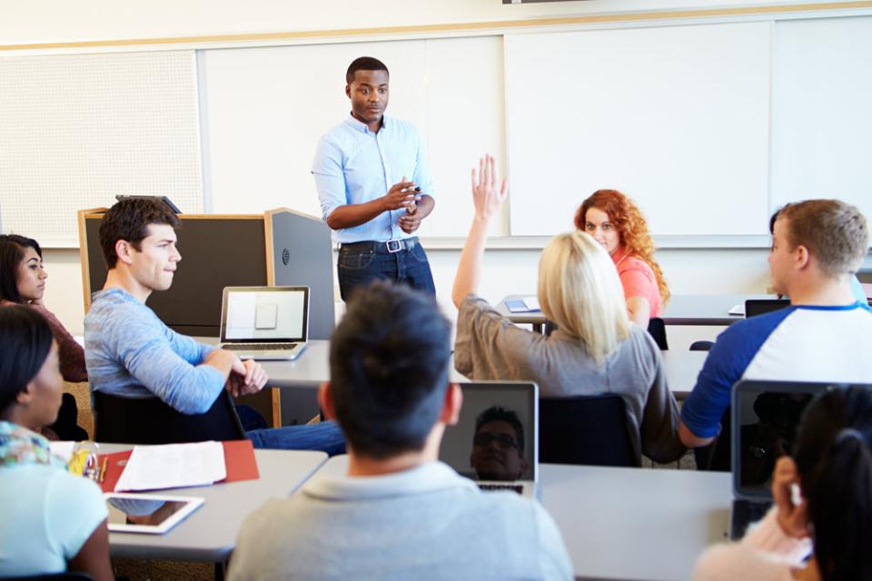A student raises her hand in the classroom and her instructor points to acknowledge her