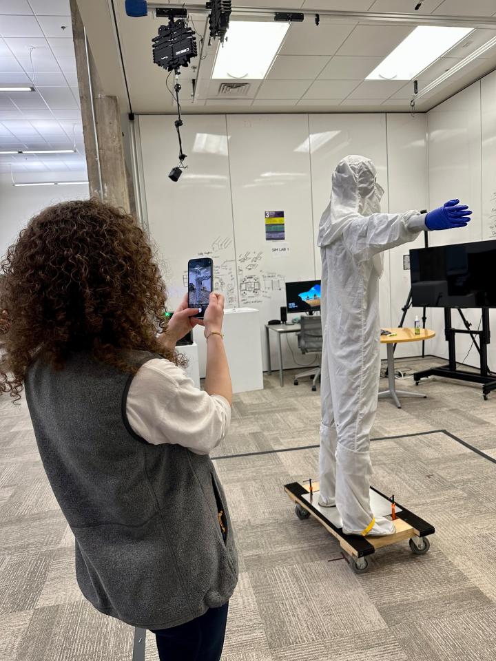 Person using a mobile device to record another person wearing a hazmat suite