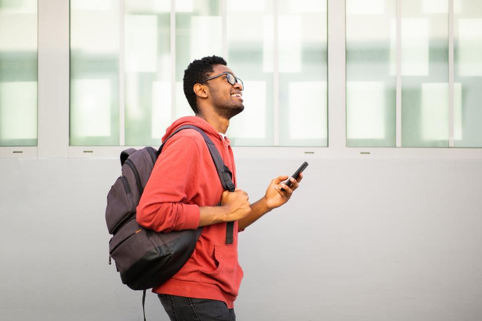 A student wearing a backpack looking at a smartphone while walking.