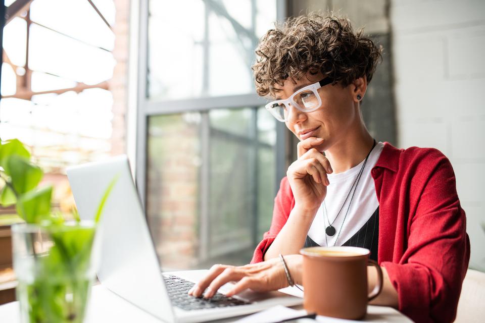 Woman working on a laptop with one hand on her chin as if she's thinking