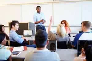 A student raises her hand in the classroom and her instructor points to acknowledge her