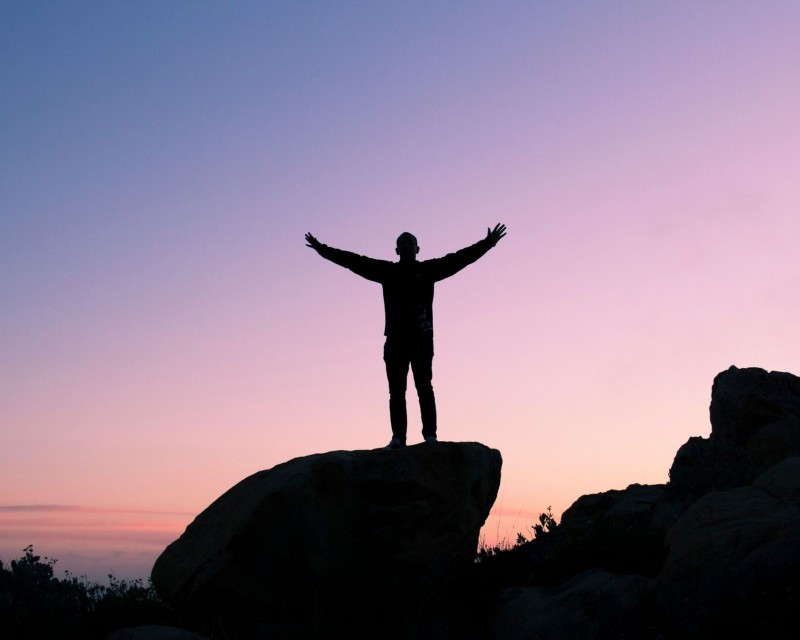 Outline of a person standing on a rock with arms outstretched.